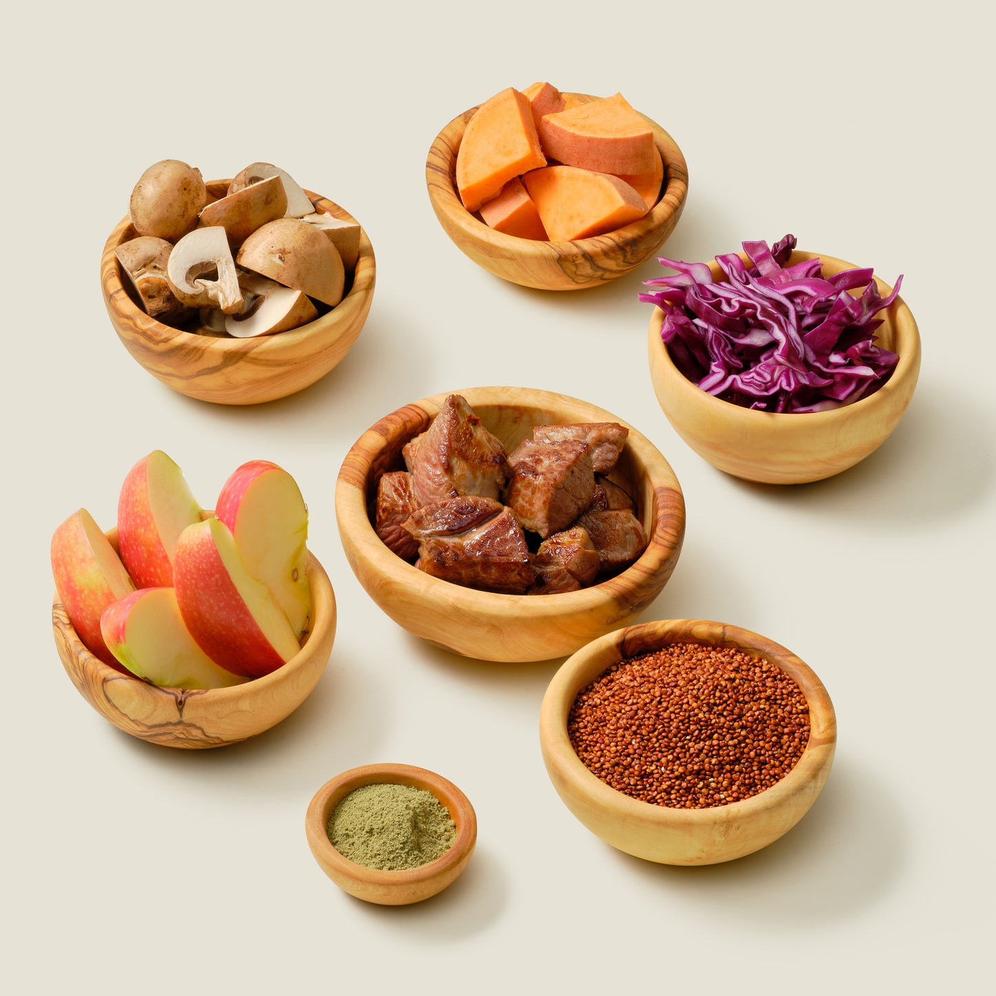 Grain-free organic dog food ingredients: Regal Lamb recipe with organic lamb, sweet potato, quinoa, cabbage, kale, olive oil, sunflower seeds, and flaxseed oil to support gut health, arranged in natural wood bowls