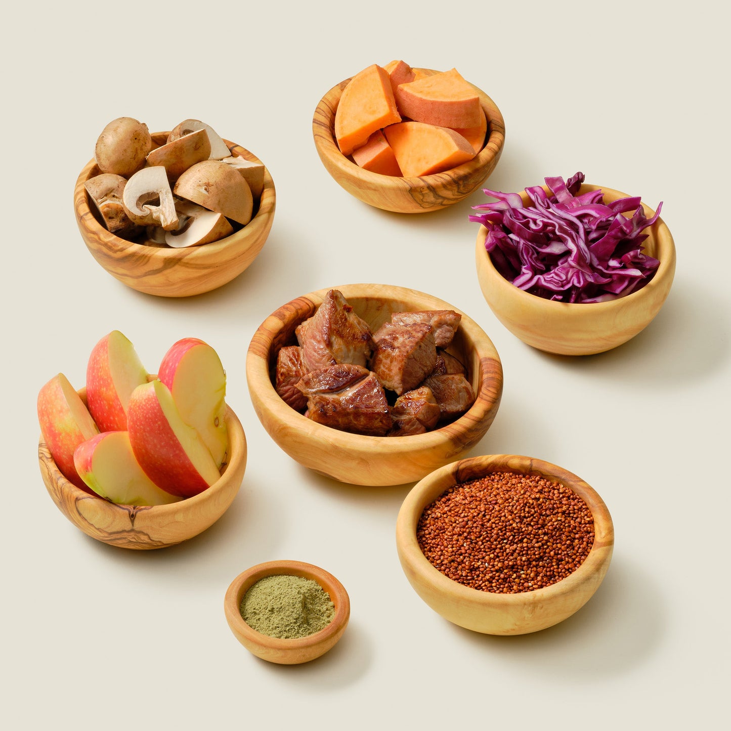 Grain-free organic dog food ingredients: Regal Lamb recipe with organic lamb, sweet potato, quinoa, cabbage, kale, olive oil, sunflower seeds, and flaxseed oil to support gut health, arranged in natural wood bowls