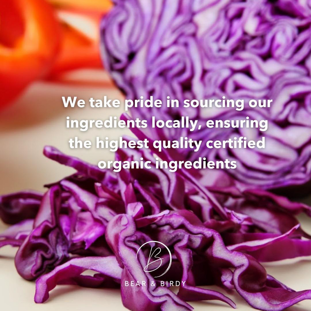 Close-up of vibrant organic red cabbage with text overlay reading “We take pride in sourcing our ingredients locally, ensuring the highest quality certified organic ingredients” – part of Bear & Birdy’s commitment to fresh, local, organic dog food.